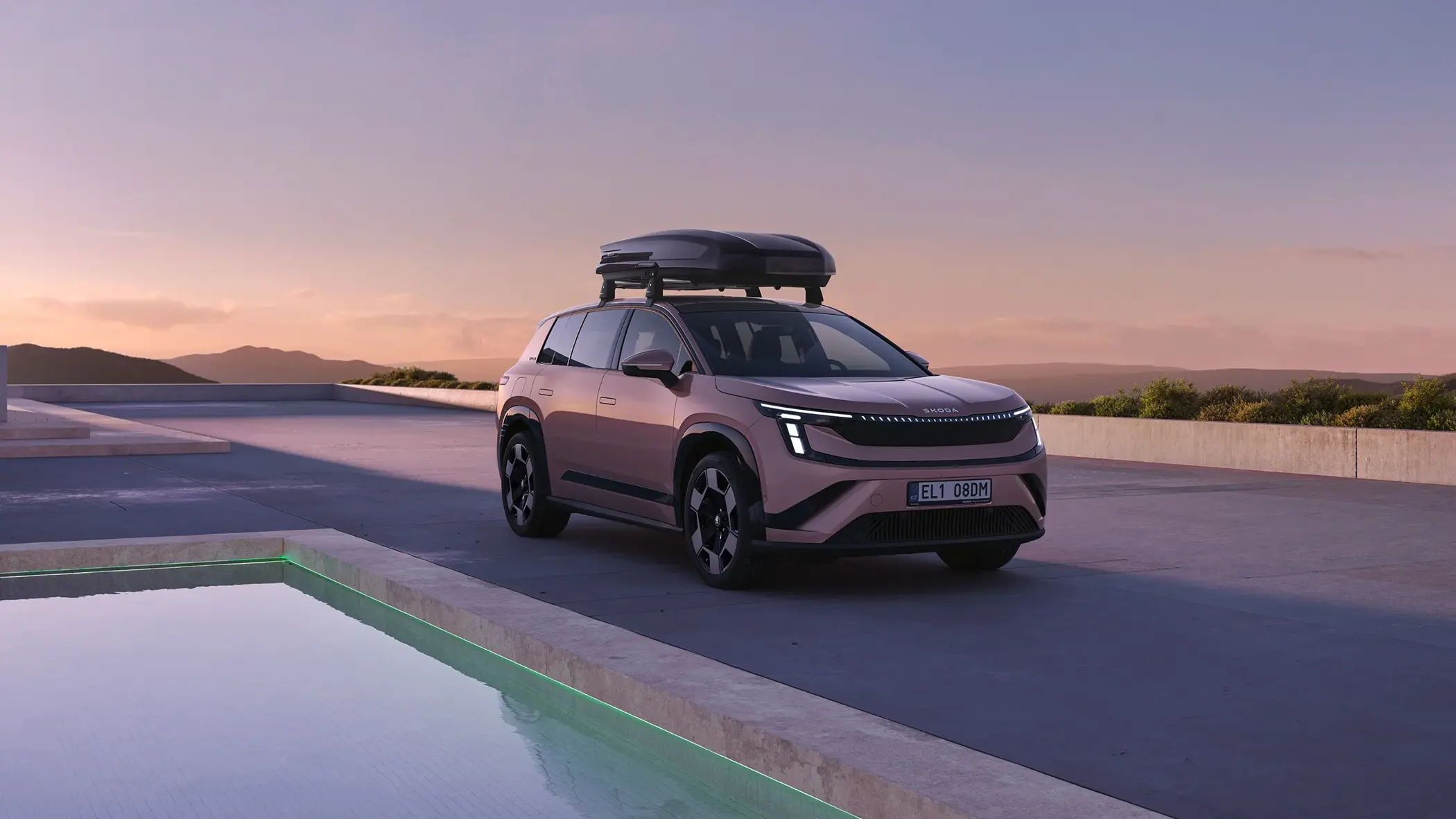 En lyserød SUV med tagboks holder parkeret ved en pool i et moderne, åbent landskab ved solnedgang.